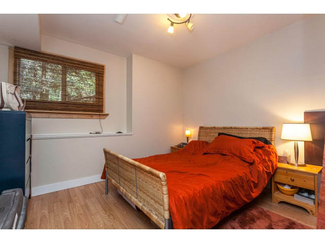 Bright bedroom with hardwood floors, red bedding, and a wicker bed frame. - 3243 Milton Ave., North Vancouver