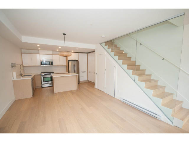 Bright kitchen with modern appliances and hardwood floors, leading to a staircase with glass railings. - 3187 St. George St., Vancouver East Side