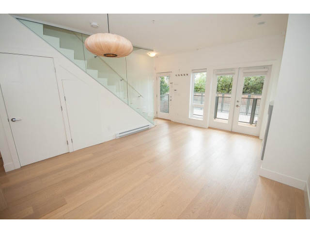 Bright living room with hardwood floors and glass staircase leading to upper level. - 3187 St. George St., Vancouver East Side