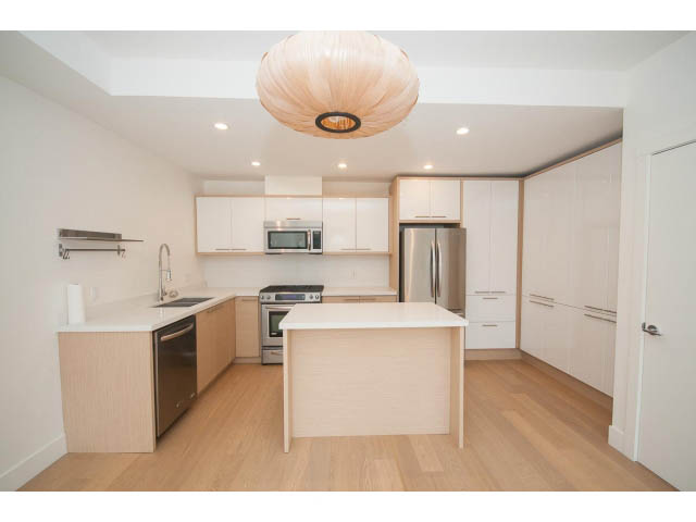Bright kitchen with light wood cabinets, stainless steel appliances, and a large island with white countertops.