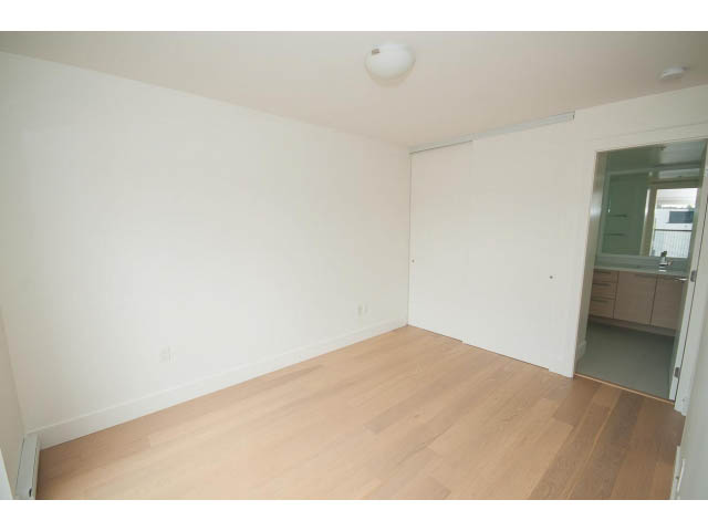 Bright living room with hardwood floors and a sliding door leading to a kitchen area. - 3187 St. George St., Vancouver East Side