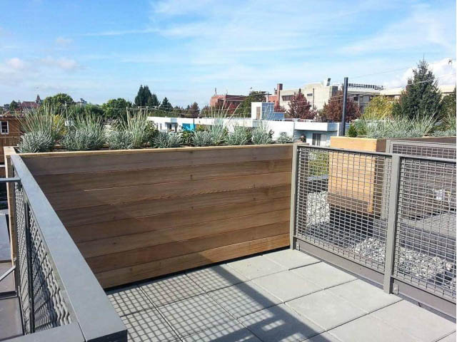 Furnished rooftop deck with wooden planter and metal railing, city view in background. - 3187 St. George St., Vancouver East Side