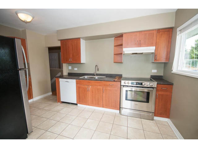 Bright kitchen with stainless steel appliances and wooden cabinets, tiled floor, and city view. - 549 W Queens, North Vancouver