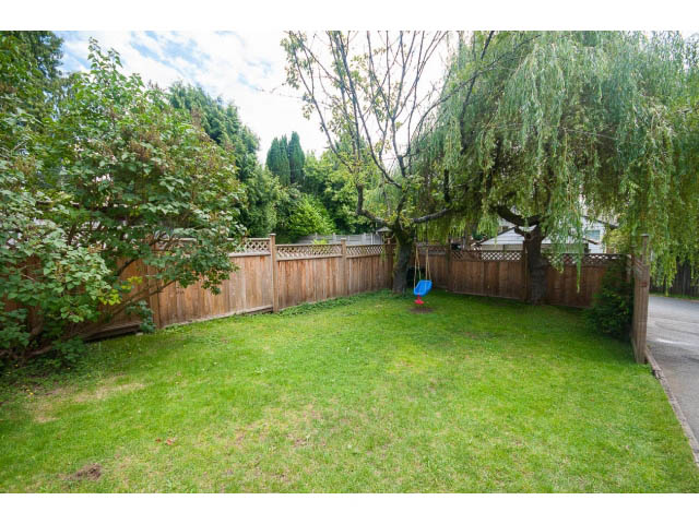 Lush green backyard with wooden fencing and a swing set. - 549 W Queens, North Vancouver
