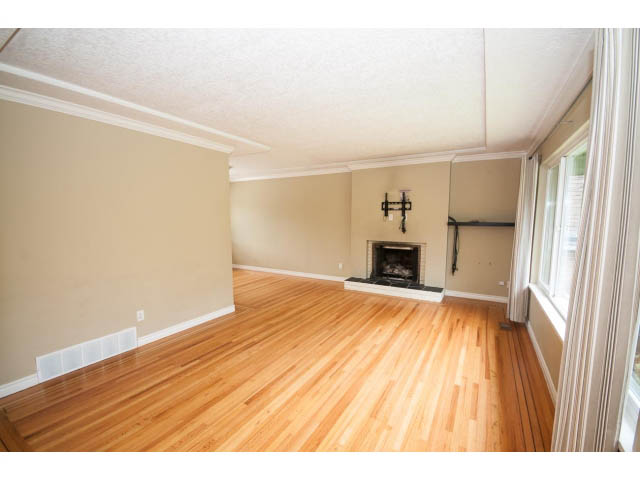 Spacious living room with hardwood floors and a fireplace, leading to a dining area. - 549 W Queens, North Vancouver