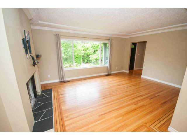 Bright living room with hardwood floors and large windows showing greenery. - 549 W Queens, North Vancouver