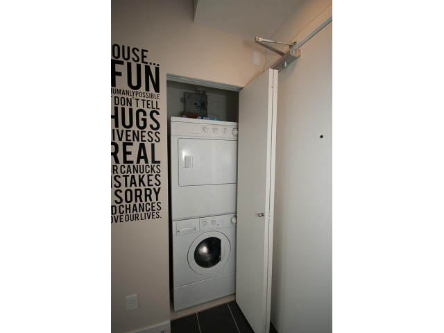 Furnished laundry room with stacked washer and dryer, white walls, and wall art. - 1105 - 175 West 2nd Street, North Vancouver