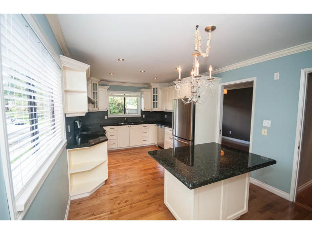 Bright kitchen with white cabinets, dark granite countertops, hardwood floors, and a chandelier. - Upper - 1998 Cortell St., North Vancouver