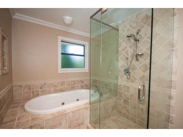 Spacious bathroom with glass shower and bathtub, beige tiles, and a frosted window. - Upper - 1998 Cortell St., North Vancouver