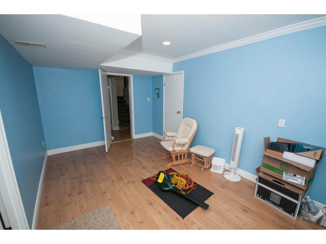 Bright living room with hardwood floors and blue walls, featuring a den area and a cozy corner with a chair and a basket.