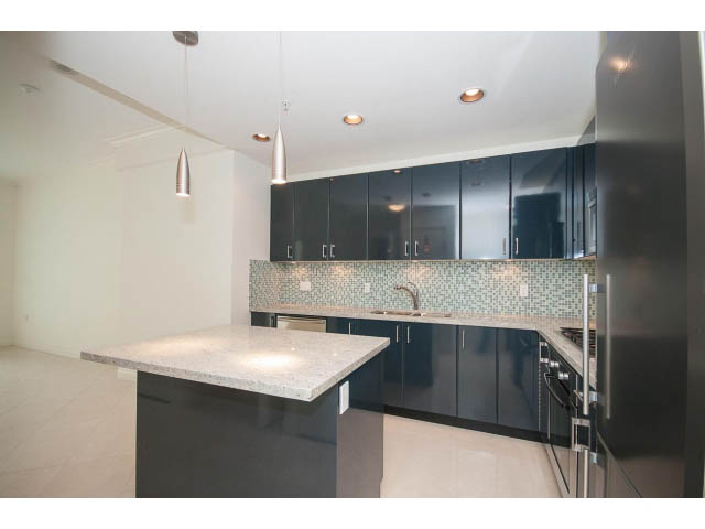Bright kitchen with black cabinets, granite countertops, and modern pendant lights. - 203 - 162 Victory Ship Way, North Vancouver