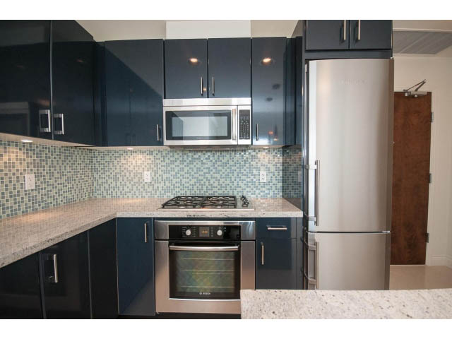 Bright kitchen with granite countertops, stainless steel appliances, and dark cabinetry. - 203 - 162 Victory Ship Way, North Vancouver