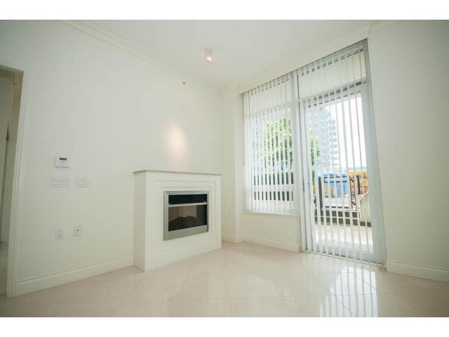 Bright living room with fireplace and sliding glass doors leading to a balcony. - 203 - 162 Victory Ship Way, North Vancouver