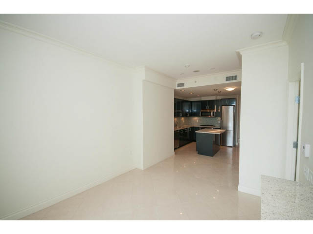 Spacious living room with glossy white floors and modern kitchen in the background. - 203 - 162 Victory Ship Way, North Vancouver