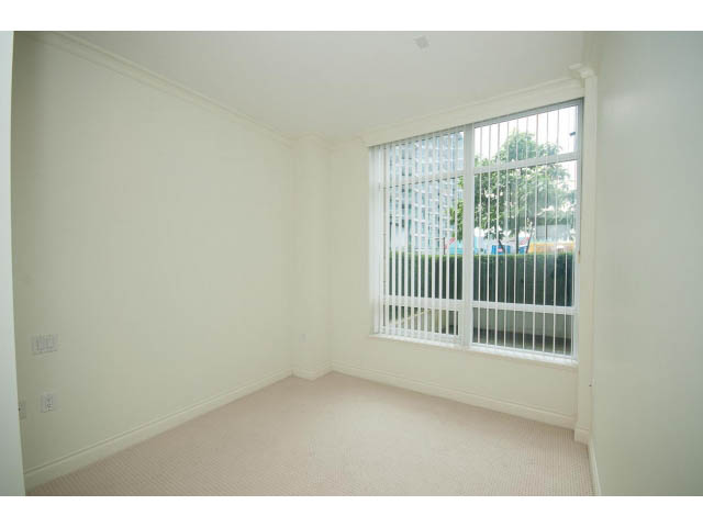 Bright living room with sliding glass door leading to a patio, white walls, and carpeted floor. - 203 - 162 Victory Ship Way, North Vancouver