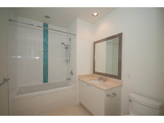 Bright bathroom with white cabinetry, marble countertops, and a bathtub/shower combo. - 203 - 162 Victory Ship Way, North Vancouver