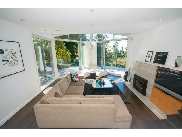 Spacious living room with large windows, hardwood floors, and a modern fireplace. - 6190 Candia Place, West Vancouver