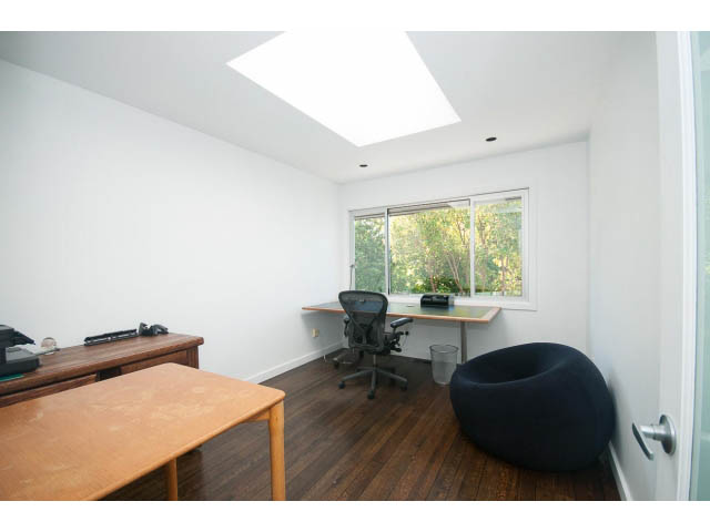 Bright home office with wooden desk, skylights, and large windows showing greenery. - 6190 Candia Place, West Vancouver