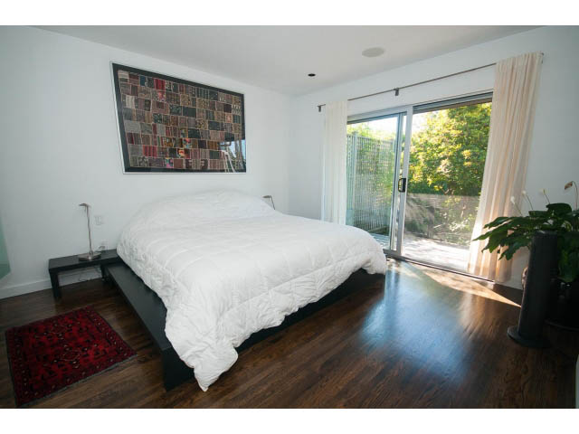 Bright bedroom with hardwood floors, large sliding glass door, and a red rug. - 6190 Candia Place, West Vancouver