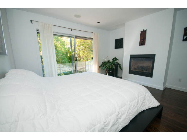 Spacious bedroom with large sliding doors, white bedding, and a cozy fireplace. - 6190 Candia Place, West Vancouver