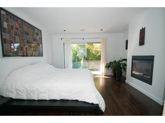 Bright bedroom with white bedding, hardwood floors, and a large window view. - 6190 Candia Place, West Vancouver