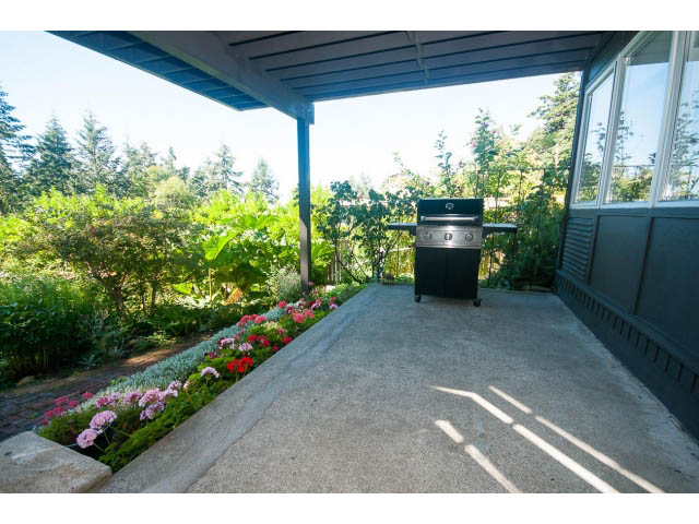 Furnished patio with built-in grill and flower beds, surrounded by greenery. - 6190 Candia Place, West Vancouver