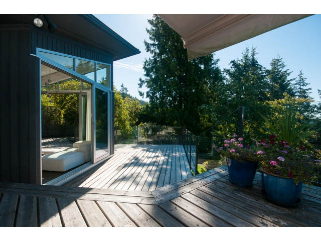 Furnished living room with large windows, wooden deck, and lush greenery view. - 6190 Candia Place, West Vancouver