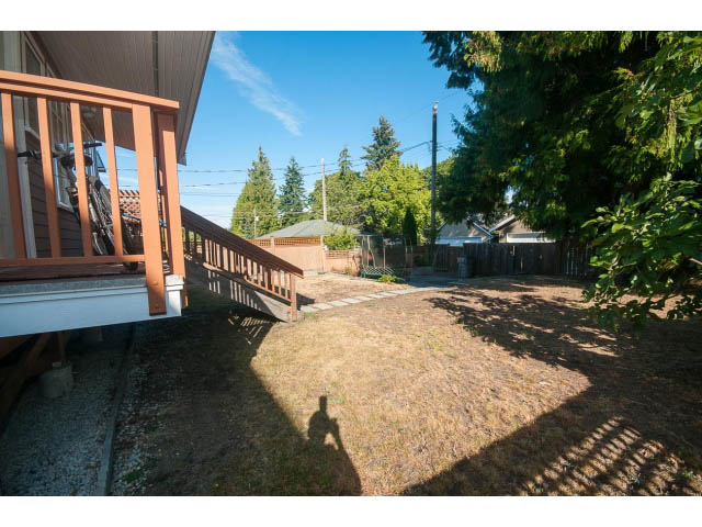 Bright patio with wooden railings and lush greenery, leading to a spacious backyard with a gravel path. - 2939 West 30th Ave, Vancouver West Side