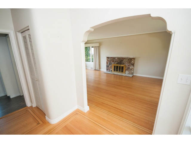 Bright living room with hardwood floors and arched fireplace, leading to another room. - 221 Carisbrooke Crescent, North Vancouver