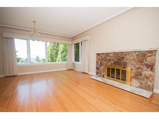 Spacious living room with hardwood floors and a stone fireplace, large windows offering a city view. - 221 Carisbrooke Crescent, North Vancouver