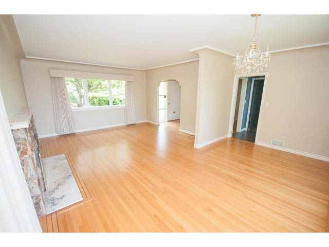 Spacious living room with hardwood floors and a fireplace, leading to a dining area with a chandelier. - 221 Carisbrooke Crescent, North Vancouver