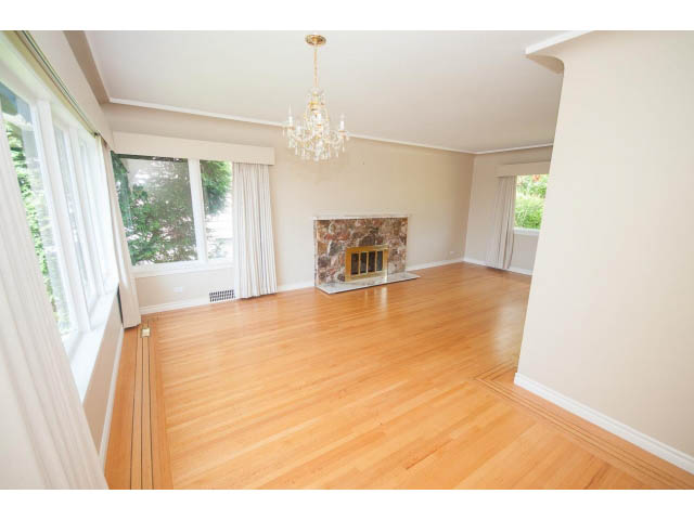 Bright living room with hardwood floors and a chandelier, leading to a cozy fireplace. - 221 Carisbrooke Crescent, North Vancouver