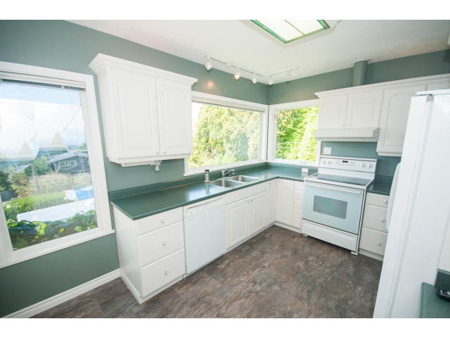 Bright kitchen with white cabinets, teal countertops, and hardwood floors, showcasing a city view through large windows.