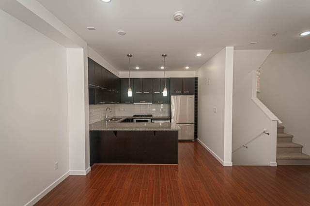 Bright kitchen with dark cabinetry and granite countertops, hardwood floors, and a view of the staircase leading to the...