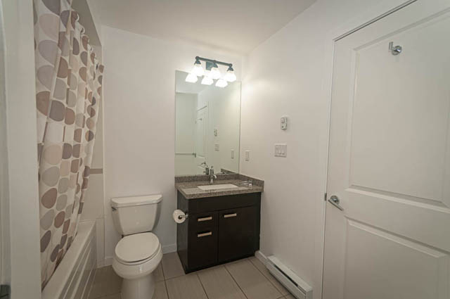 Bright bathroom with modern vanity, white walls, and a shower curtain. - 2753 Guelph Street, Vancouver East Side