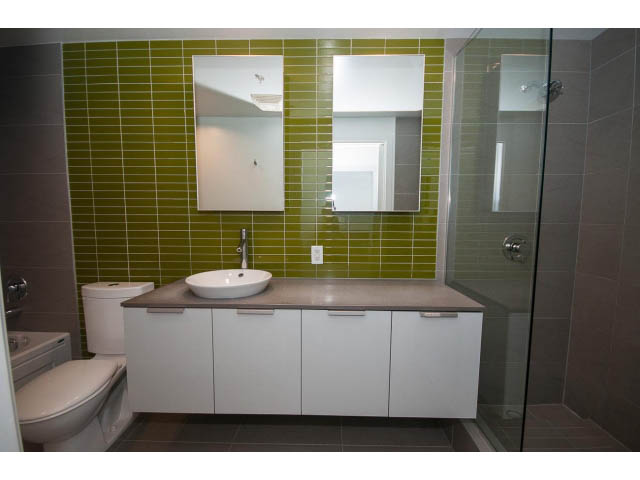 Modern bathroom with green tiles, white cabinets, and a glass shower. - 803 - 128 Cordova St W, Vancouver Downtown