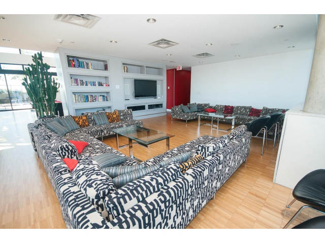 Spacious living room with patterned sofas, hardwood floors, and a large TV. - 803 - 128 Cordova St W, Vancouver Downtown