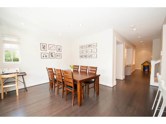 Bright dining area with wooden chairs and hardwood floors, leading to a kitchen with white countertops. - 26 - 555 Raven Woods Drive, North Vancouver
