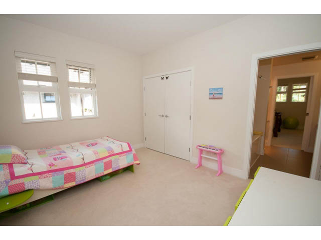 Bright bedroom with patchwork quilt, white walls, and a window. - 26 - 555 Raven Woods Drive, North Vancouver
