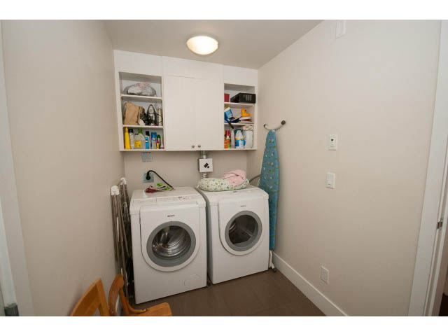 Laundry room with stacked washer and dryer, shelves, and hanging towel. - 26 - 555 Raven Woods Drive, North Vancouver