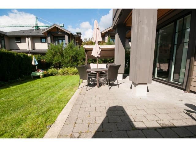 Furnished patio with outdoor furniture and umbrella, leading to a grassy backyard. - 26 - 555 Raven Woods Drive, North Vancouver