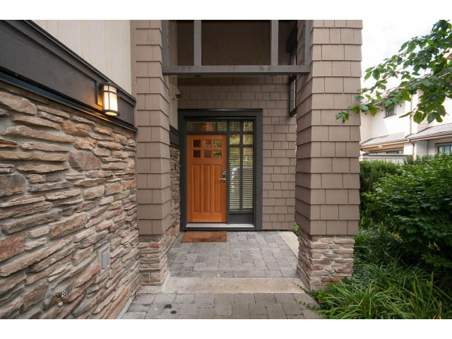 Entryway with stone walls and wooden door, leading to a paved patio. - 26 - 555 Raven Woods Drive, North Vancouver