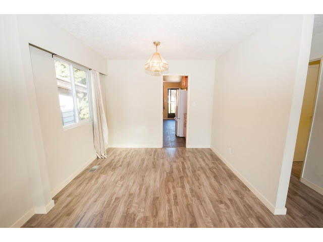Bright living room with hardwood floors and a chandelier, leading to a kitchen area. - 1730 Bowser Ave., North Vancouver