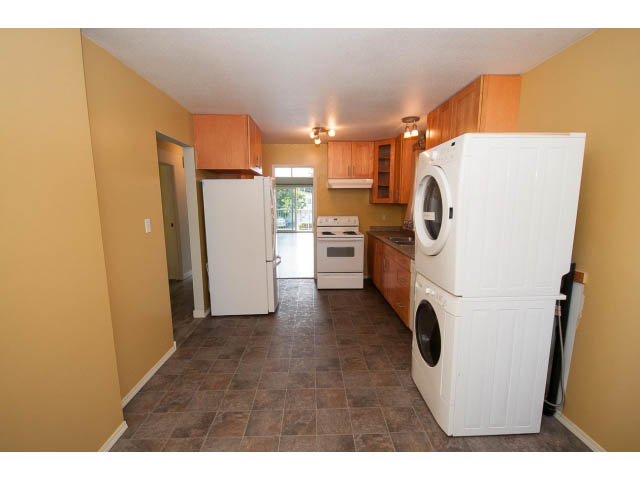 Shared kitchen with white appliances and brown cabinets, tiled floor. - 1730 Bowser Ave., North Vancouver