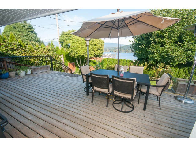 Furnished patio with wooden deck, outdoor furniture, and umbrella, overlooking greenery and water. - 389 Beachview Dr, North Vancouver