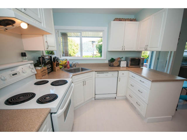 Bright kitchen with white cabinets, beige countertops, and a view of greenery outside. - 389 Beachview Dr, North Vancouver