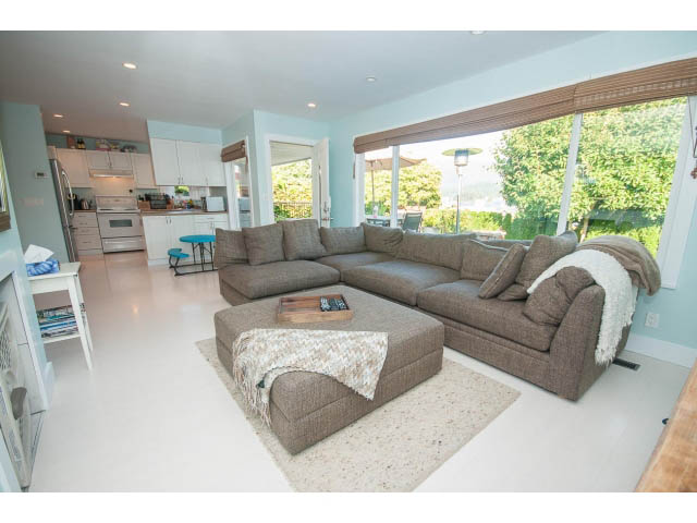 Spacious living room with large sectional sofa, hardwood floors, and a view of greenery outside. - 389 Beachview Dr, North Vancouver