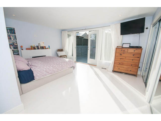 Bright bedroom with white walls, wooden dresser, sliding glass door, and built-in bookshelf. - 389 Beachview Dr, North Vancouver