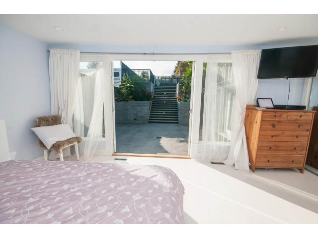 Spacious bedroom with large windows, beach view, and wooden furniture. - 389 Beachview Dr, North Vancouver