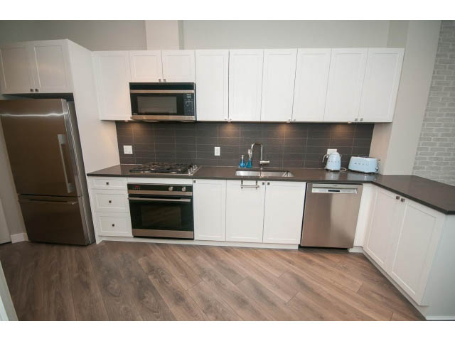 Bright kitchen with white cabinets, stainless steel appliances, and hardwood floors. - 405 - 105 West 2nd St, North Vancouver